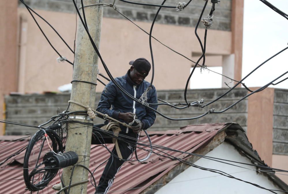 A man connects electric cables above the Kibera informal settlement in Nairobi, Kenya
